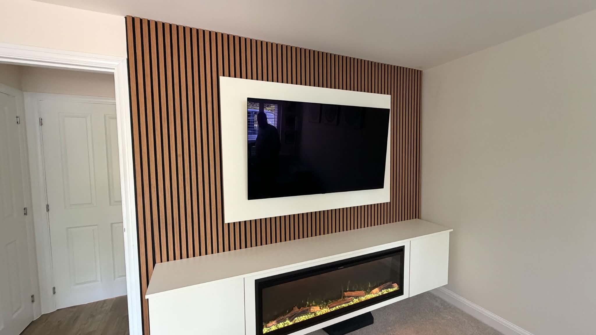 Media wall with integrated electric fireplace, slatted panels and downlit niches